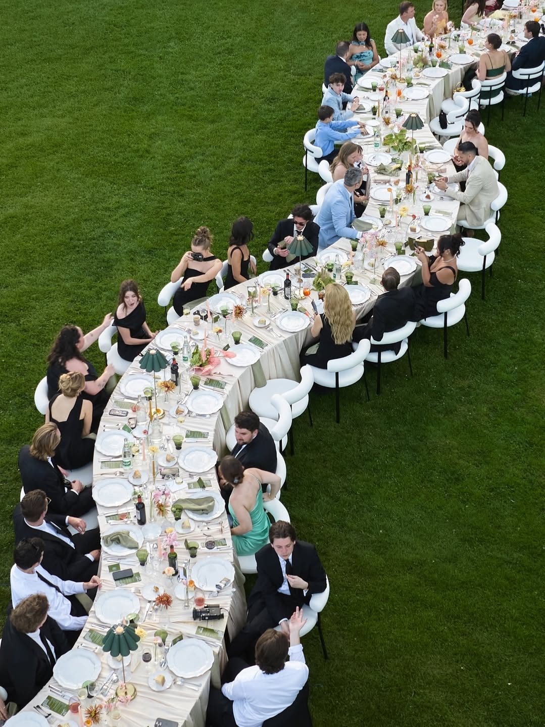 Une longue table de banquet sur la pelouse, vue du ciel, les convives attablés