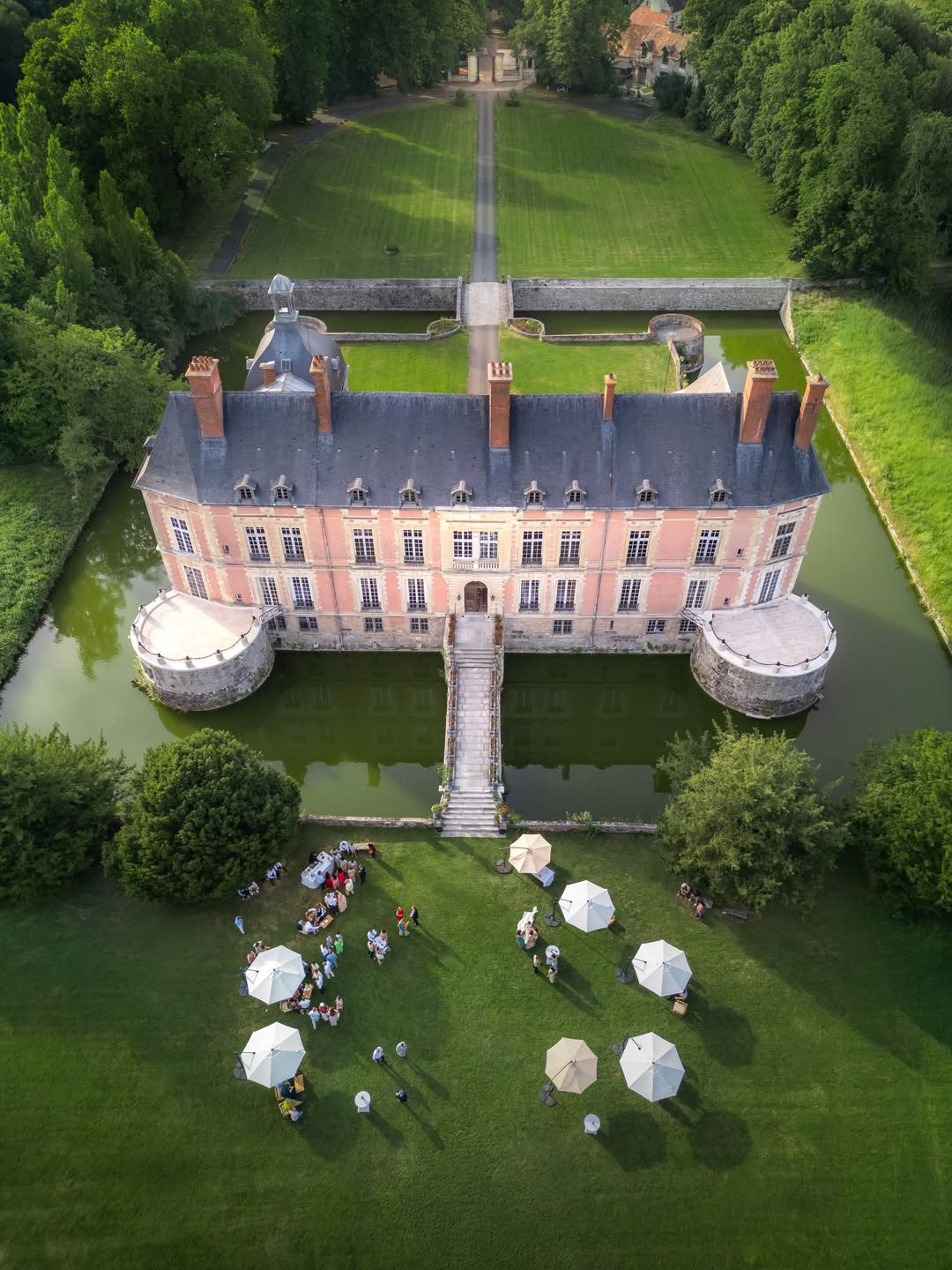 Le château et ses douves vus du ciel, une réception installée sur la pelouse