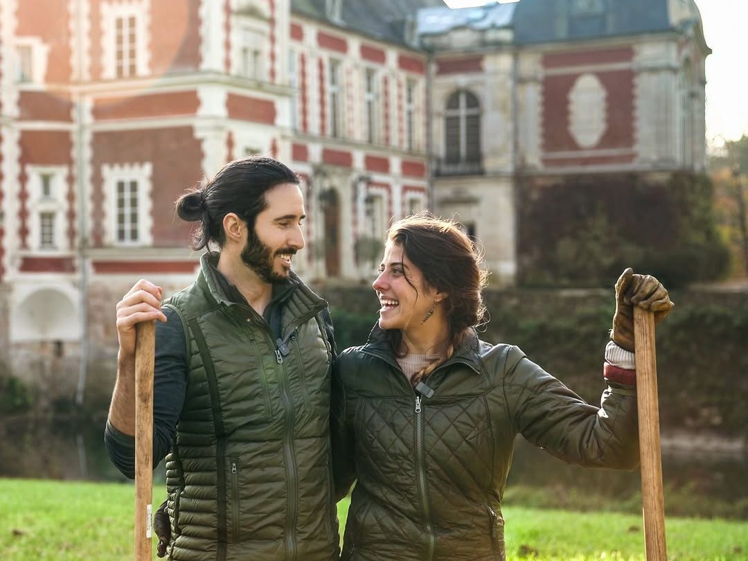 Deux membres de la famille, outils à la main, devant la façade du château
