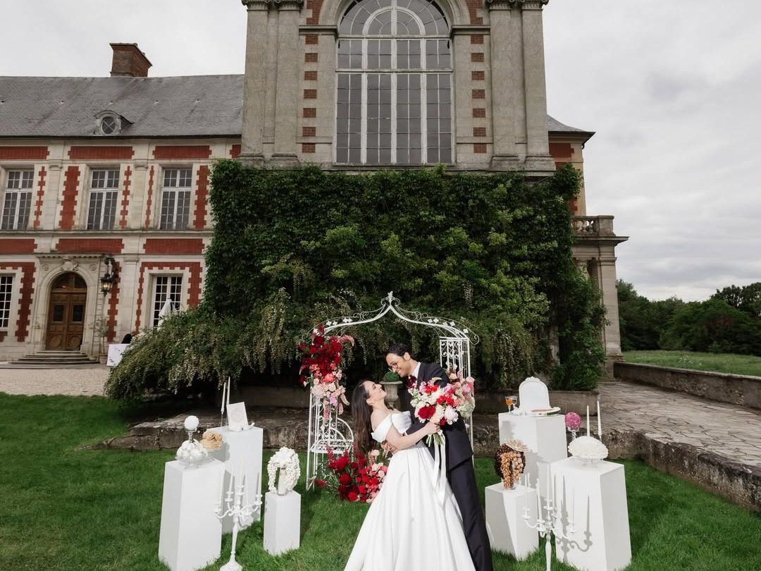 Les mariés sous l'arche florale, la façade du château derrière eux